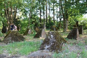 Panzersperren der Höckerlinie, umgeben von Grass und Bäumen, am linken Rand zwei Schüler:innen.