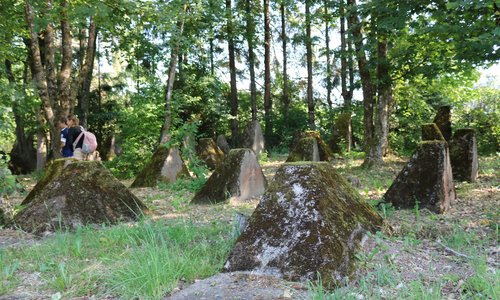 Panzersperren der Höckerlinie, umgeben von Grass und Bäumen, am linken Rand zwei Schüler:innen.