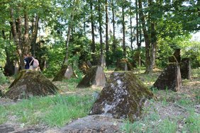 Panzersperren der Höckerlinie, umgeben von Grass und Bäumen, am linken Rand zwei Schüler:innen.