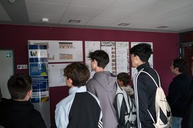 Einige Schüler betrachten Baupläne, die an der Wand hängen.